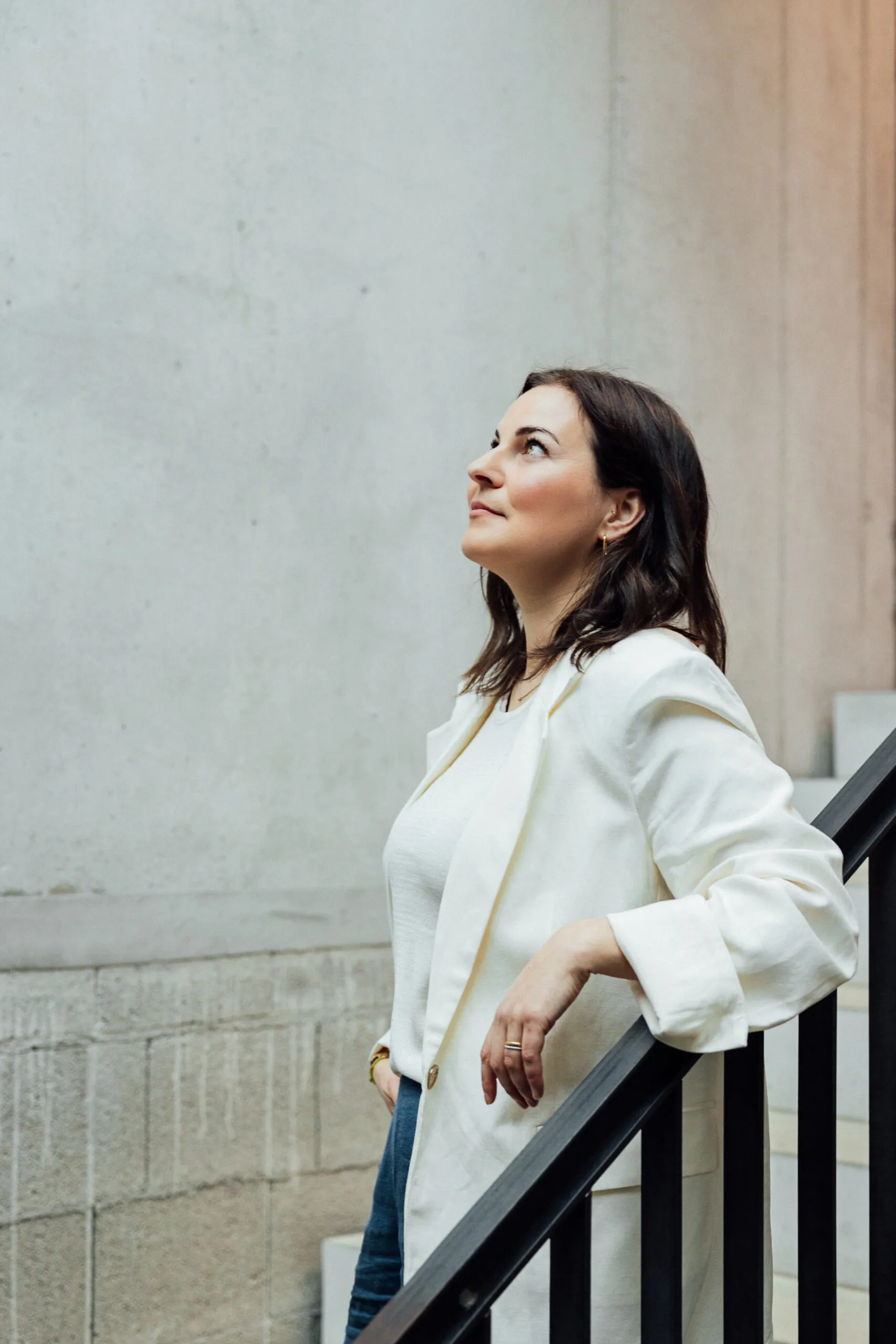 Julia Bechter in weißer Bluse am Treppengeländer, der Blick geht nach oben